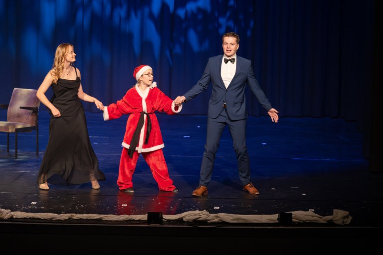 Drei Performer auf Bühne: Frau im schwarzen Kleid, Kind im Nikolaus-Kostüm und Mann im Anzug mit Fliege.