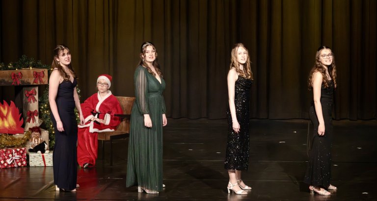 Fünf Sängerinnen in eleganten Kleidern und eine als Nikolaus verkleidete Person auf der Weihnachtsbühne der Musicalschule Ahrensburg.