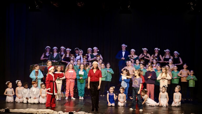 Adventsshow der Musicalschule Ahrensburg mit Kindern in Weihnachtskostümen, Elisabeth Hübert im roten Outfit auf der Bühne.
