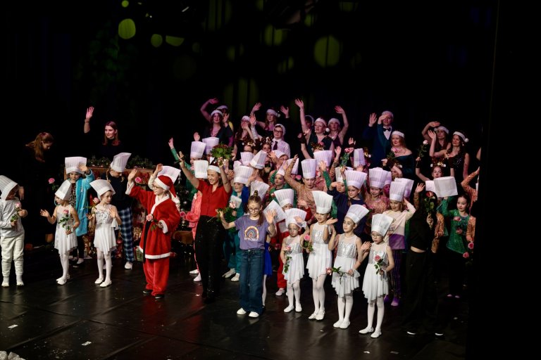 Große Gruppe von Kindern und Erwachsenen auf der Bühne in weihnachtlichen Kostümen und Nikolaus-Mützen während der Adventsshow.