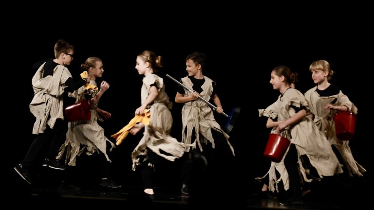 Kinder in Piraten-Kostümen führen musikalische Szene mit Instrumenten und roten Eimern auf schwarzer Bühne auf.