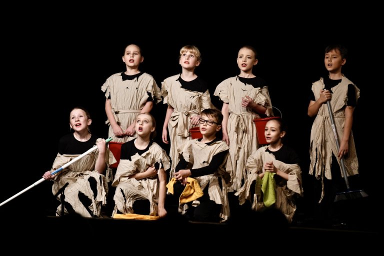 Kindertheatergruppe auf Bühne in beige Kostümen singt gemeinsam, "All Together Now" Musicalschule Ahrensburg Performance.