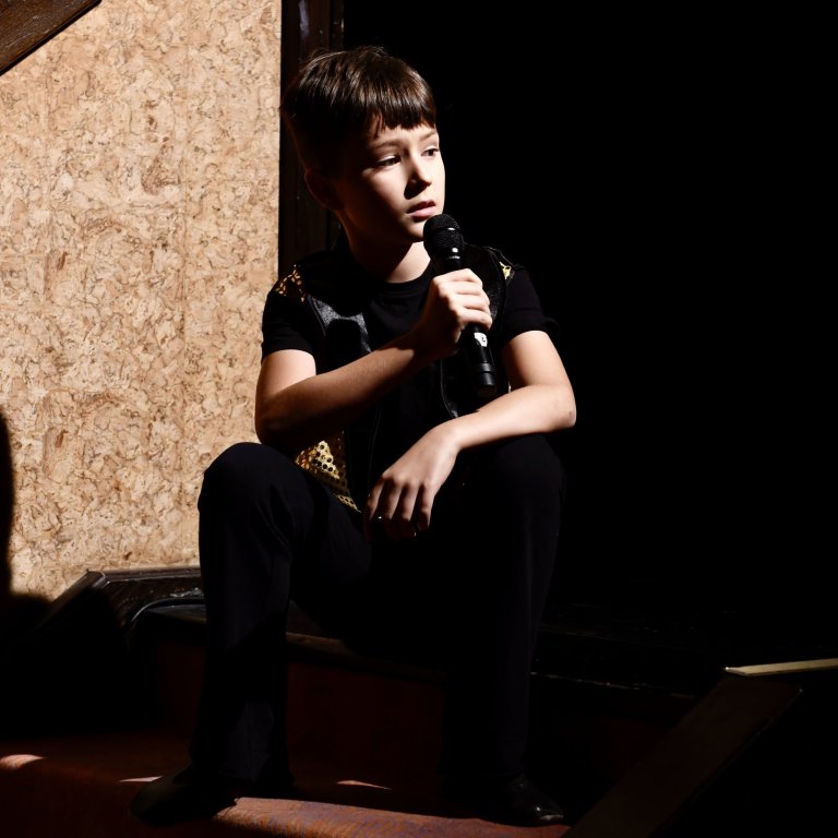Junge Sängerin mit Mikrofon auf Bühne sitzt während Musikaufführung, Musicalschule Ahrensburg Auftritt.
