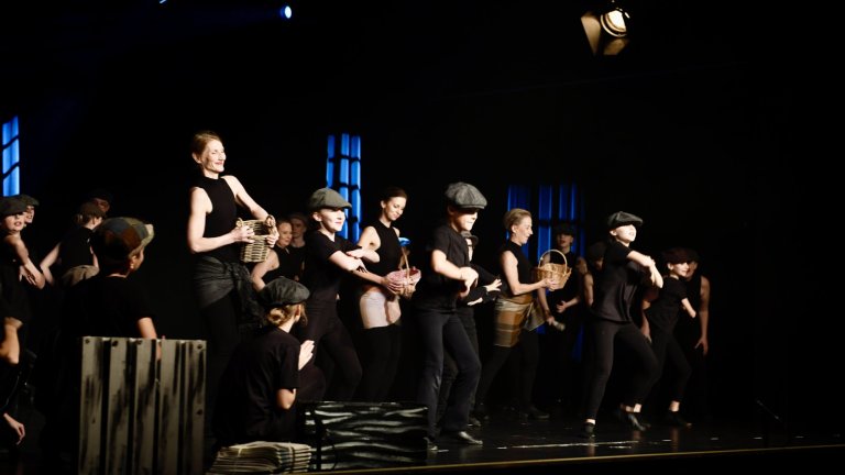 Musicalschule-Ensemble in schwarzer Kleidung und Mützen performt mit Percussionsinstrumenten auf Bühne.