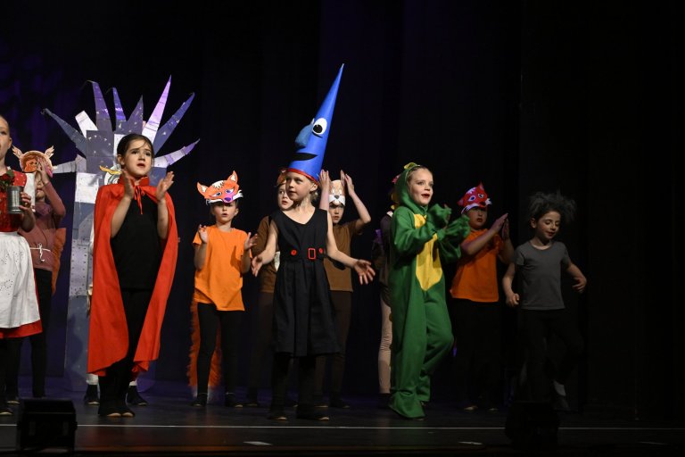 Kinder in bunten Kostümen und Masken performen auf der Bühne der Musicalschule Ahrensburg Jubiläumsshow.