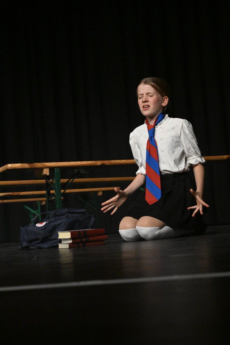 Junger Schüler in weißem Hemd und rot-blauer Krawatte performt ausdrucksstark auf der Bühne der Musicalschule Ahrensburg.