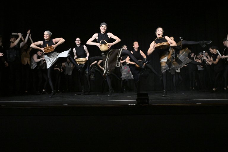 Ensemble der Musicalschule Ahrensburg performt auf Bühne mit Körben, schwarz gekleidet, fröhlich tanzend.