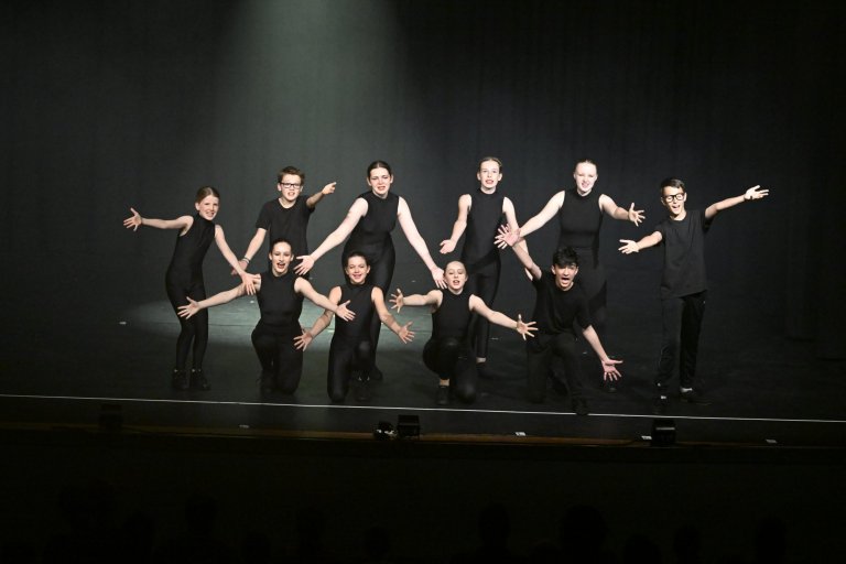 Jubiläumsshow MSA10: Gruppe junger Performer in schwarzer Kleidung posiert energiegeladen auf der Theaterbühne.