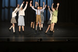 Gruppe junger Schüler springt mit erhobenen Armen auf Bühne, vintage Kostüme, Jubiläumsshow Musicalschule Ahrensburg.