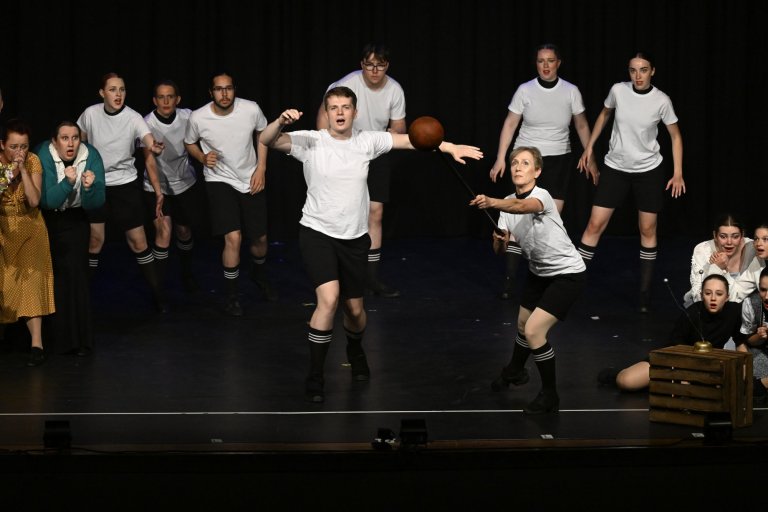 Musicalschule Ahrensburg Jubiläumsshow: Ensemble in weißen Shirts spielt Basketball-Szene auf Bühne.