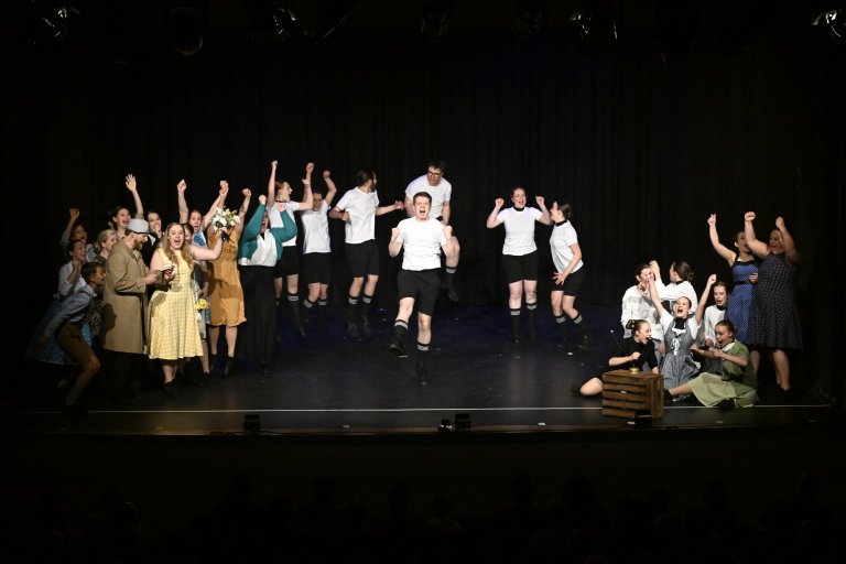 Musicalschule Ahrensburg Jubiläumsshow: Ensemble mit Kindern und Erwachsenen in Kostümen auf Bühne, alle mit erhobenen Armen.