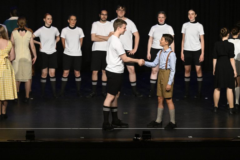 Theaterszene MSA10-Jubiläumsshow: Junge Darsteller in Sportkleidung und Vintage-Kostümen auf der Bühne interagierend.