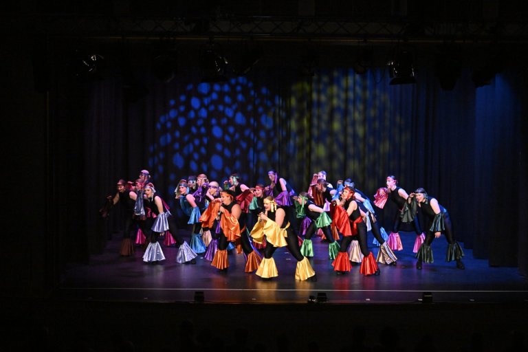 Große Ensemble-Gruppe auf Bühne in bunten Kostümen performt energiegeladene Tanznummer zur MSA10-Jubiläumsshow.