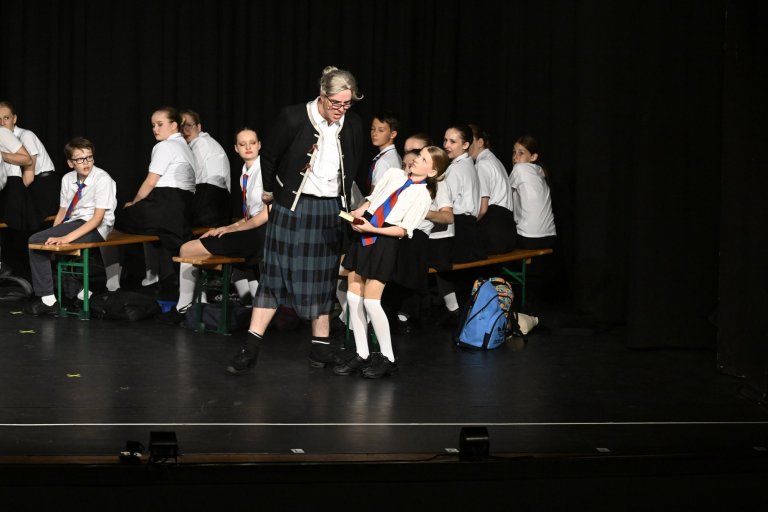 Schüler und Lehrer der Musicalschule Ahrensburg auf Bühne während Jubiläumsshow MSA10 mit Schuluniformen und Medaillen.