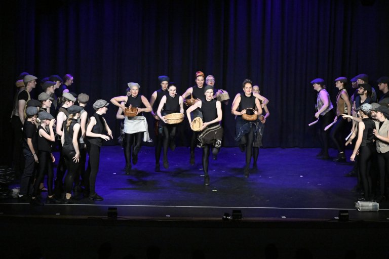 Musicalschule Ahrensburg Jubiläumsshow MSA10 mit Ensemble auf Bühne, Körbe tragend, blaue Beleuchtung, Gruppenszene.