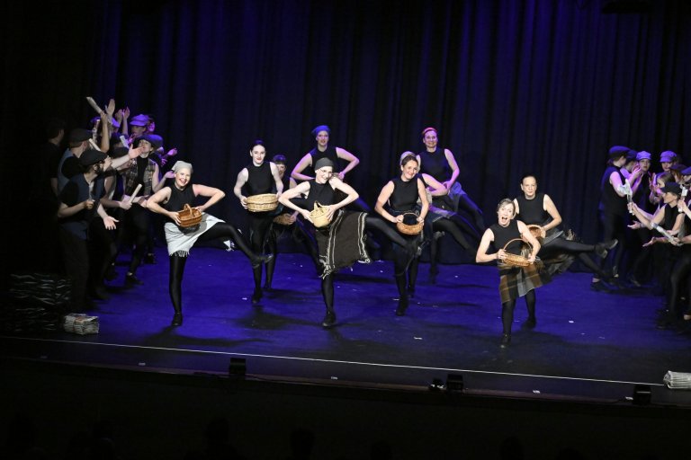 Darsteller der Musicalschule Ahrensburg präsentieren Jubiläumsshow mit Körben und Tänzern auf beleuchteter Bühne.
