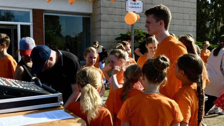 Gruppe Kinder in orangenen T-Shirts beim MSA Sommerfest 2022, versammelt vor Schulgebäude bei Aktivitäten.