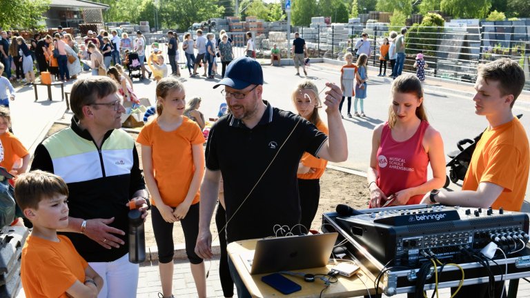 Sommerfest der Musicalschule Ahrensburg mit DJ, Kindern in orangenen Shirts und Publikum auf Außengelände.