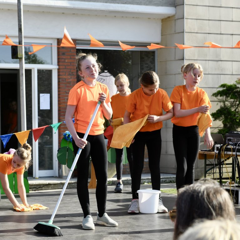 Kinder in orangefarbenen Shirts führen Tanzperformance beim MSA Sommerfest 2022 auf Schulhof auf.