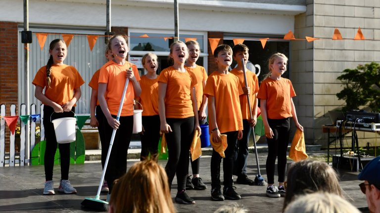 Kinder in orangenen Shirts singen beim MSA Sommerfest 2022 auf einer Außenbühne vor Publikum.