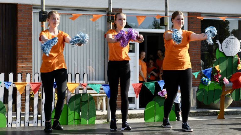 Drei junge Tänzerinnen in orangenen Shirts führen synchrone Choreographie mit blauen und lila Pompoms beim MSA Sommerfest auf.