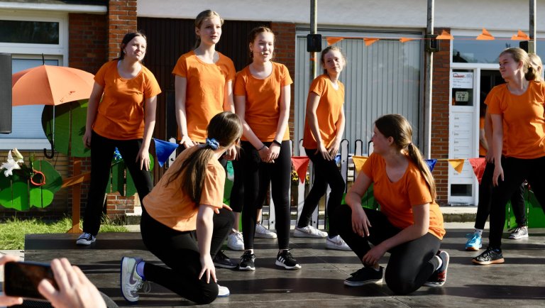 Musicalschüler in orangenen Shirts beim Sommerfest 2022 der Musicalschule Ahrensburg auf einer Bühne.