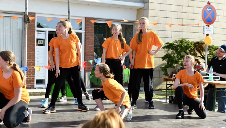 Junge Darsteller in orangen Shirts performen beim MSA Sommerfest 2022 auf einem Schulhof vor Publikum.