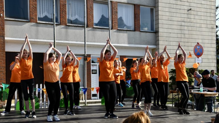 Tanzgruppe in orangen Shirts führt Choreografie beim MSA Sommerfest 2022 auf Schulhof auf.