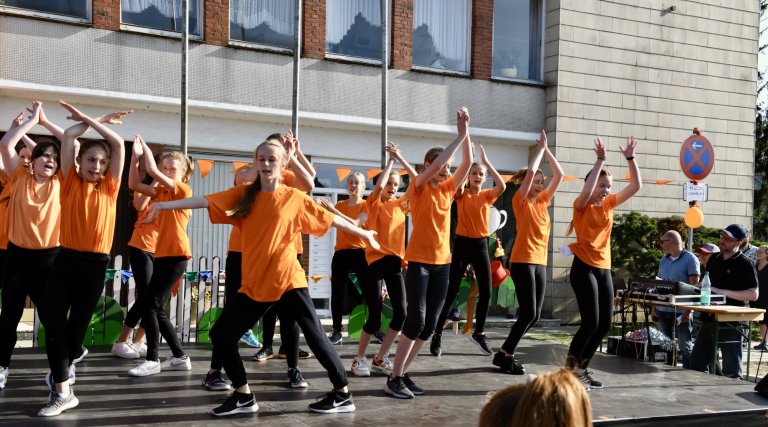 Tanzgruppe in orangenen Shirts performt choreographiertes Tanzstück beim MSA Sommerfest 2022 vor Publikum.