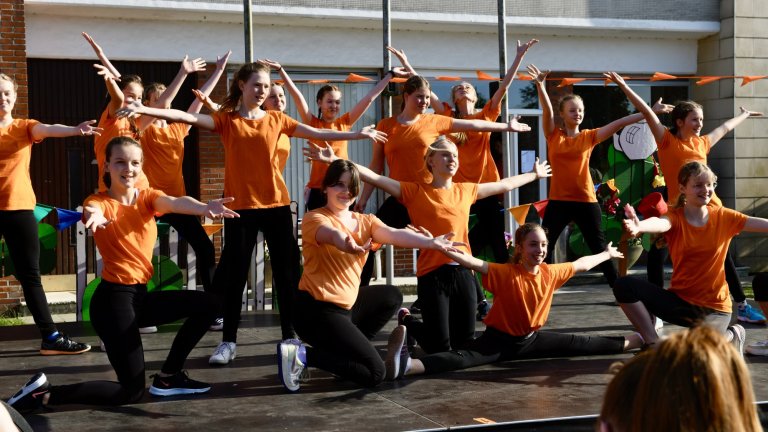 Tanzgruppe in orangenen Shirts beim Sommerfest 2022 der Musicalschule Ahrensburg, dynamische Choreografie auf Schulhof.