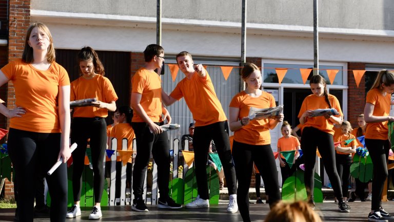 Gruppe von Kindern in orangenen T-Shirts bei Musicalschule-Sommerfest 2022 Auftritt auf Bühne.