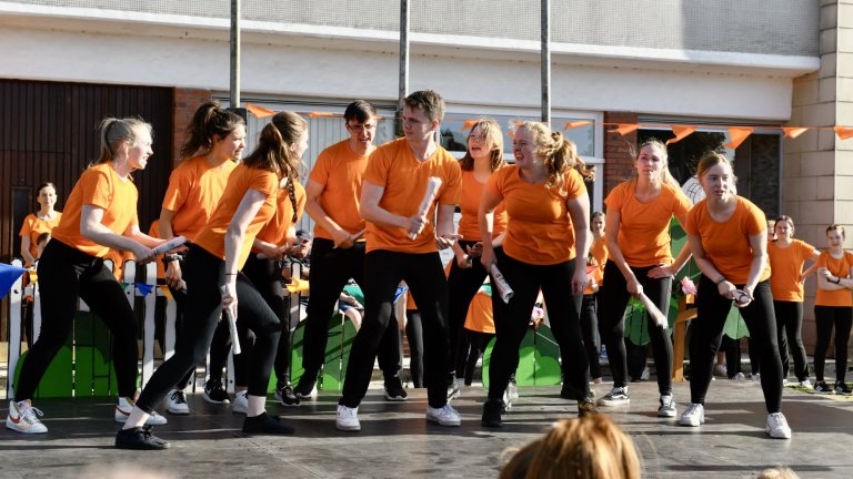Tanzgruppe in orangefarbenen Shirts performt beim MSA Sommerfest 2022 auf dem Schulhof.