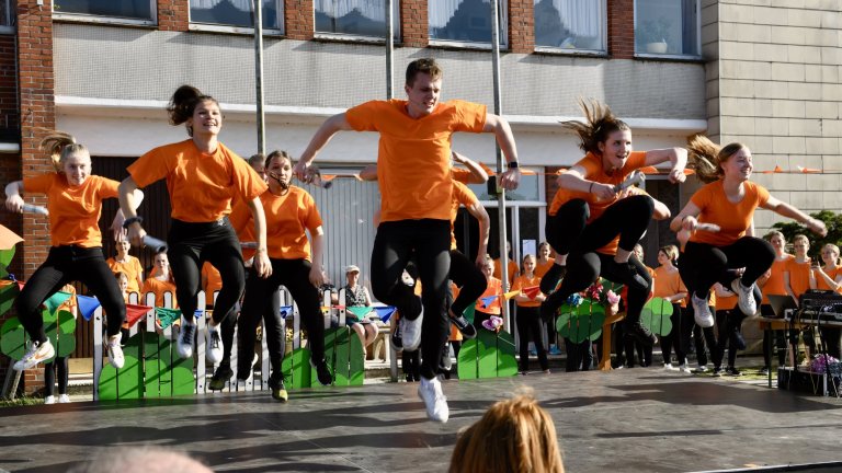 Tanzgruppe in orangen Shirts springt synchron beim MSA Sommerfest 2022 vor Publikum in Schulhof auf.