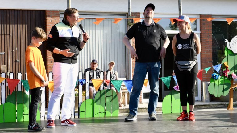 Moderator mit Mikrofon präsentiert Teilnehmer beim MSA Sommerfest 2022 auf festlich dekorierter Bühne.