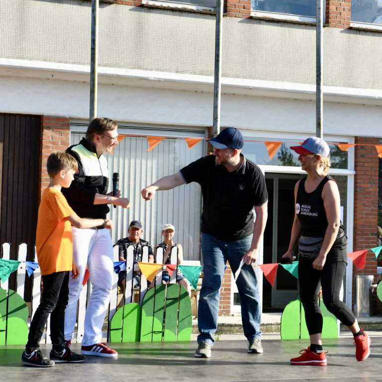 Musicalschule Ahrensburg Sommerfest 2022: Tanztrainer unterrichtet Kinder beim Outdoor-Workshop vor dekoriertem Schulgebäude.