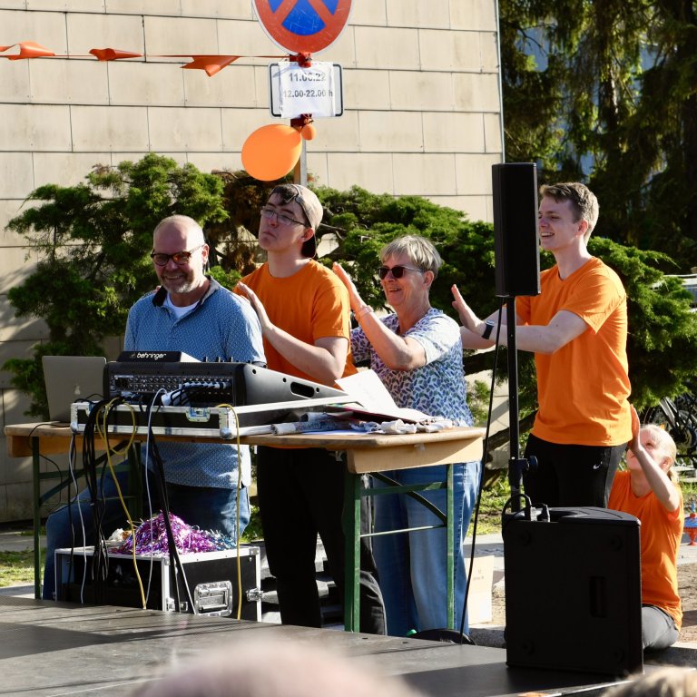 Musicalschule Ahrensburg Sommerfest 2022: Moderator und Performer in orangenen Shirts beim Bühnenprogramm vor Publikum.
