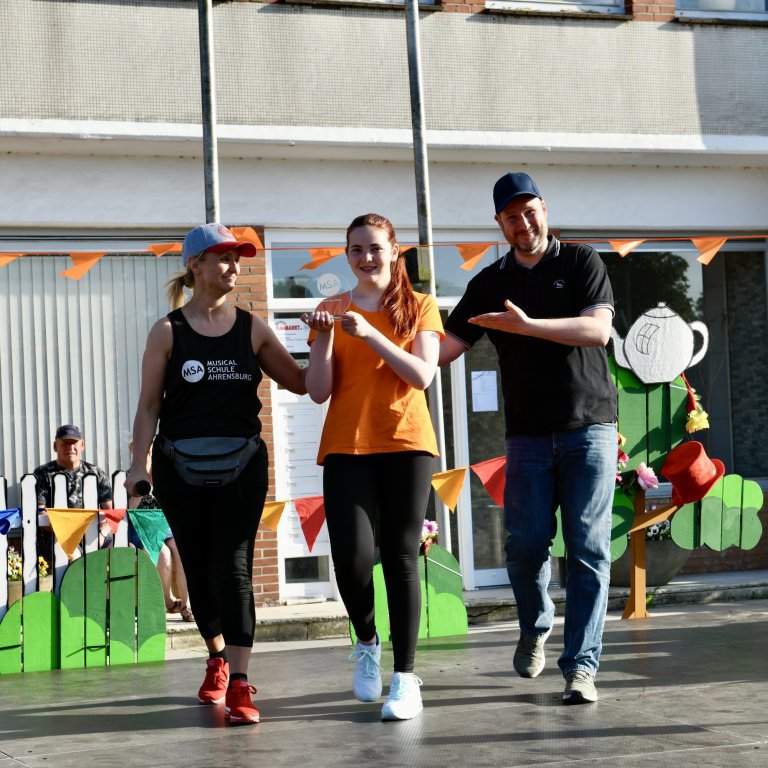 Drei Läufer beim MSA Sommerfest 2022: Zwei Mädchen und ein Mann joggen lachend vor bunten Dekorationen.
