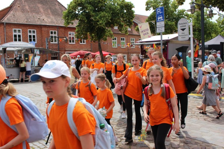 Gruppe von Kindern in orangefarbenen Shirts beim Lindenfest Ludwigslust auf Marktplatz mit historischen Gebäuden.