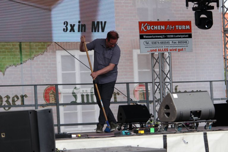 Mann führt Showtanz mit Spaten auf Bühne während Lindenfest Ludwigslust auf, humorvolle Performance.
