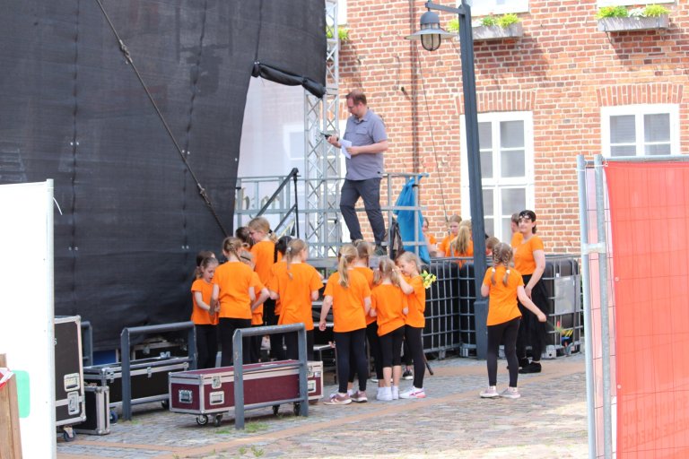 Musicalschüler in orangenen Shirts beim Lindenfest Ludwigslust auf einer Bühne mit Instruktor und Bühnentechnik.