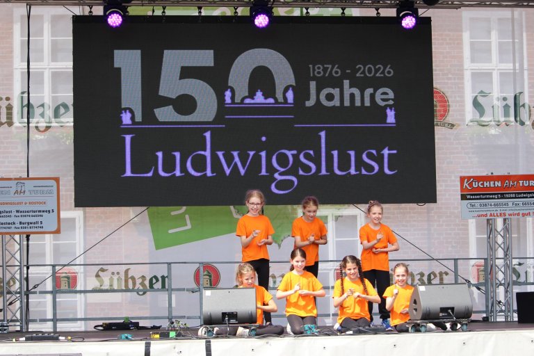 Kinder in orange und gelben Shirts performen auf Bühne zum 150-jährigen Ludwigslust-Jubiläum.