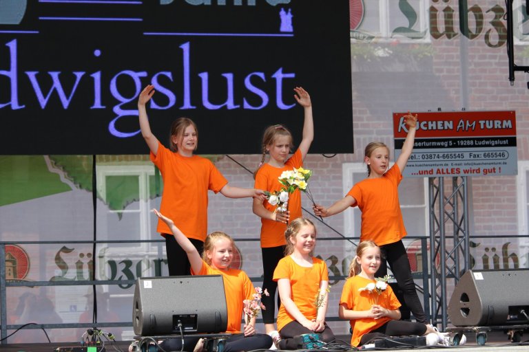 Kinder in orangefarbenen Shirts führen Tanzperformance beim Lindenfest Ludwigslust auf der Bühne auf.