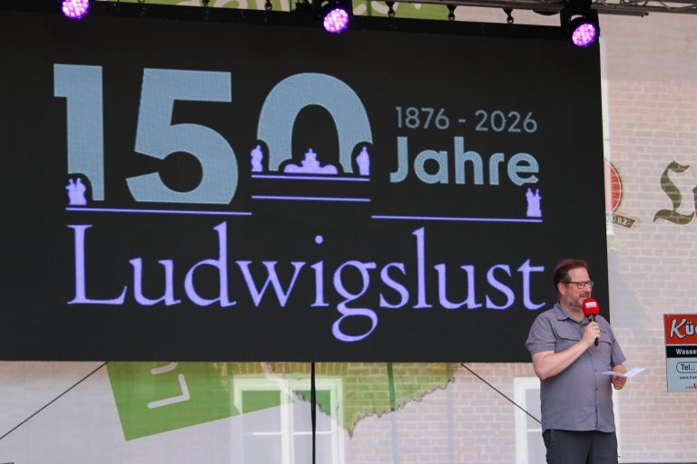 Mann mit Mikrofon präsentiert 150 Jahre Ludwigslust Jubiläum 1876-2026 auf großer Bühne.