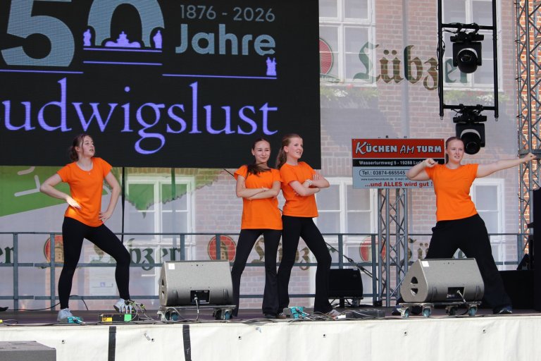 Vier Tänzerinnen in orangefarbenen Shirts performen auf Bühne zum 150-Jahr-Jubiläum Ludwigslust.