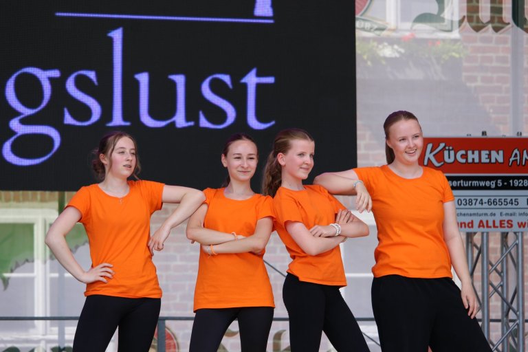Vier junge Tänzerinnen in orangenen Shirts präsentieren sich auf der Lindenfest-Bühne in Ludwigslust.