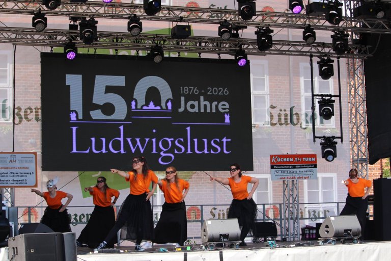 Tanzgruppe in orangenen Shirts führt Choreografie auf Bühne des Ludwigslust 150-Jahre-Jubiläumsfestes auf.