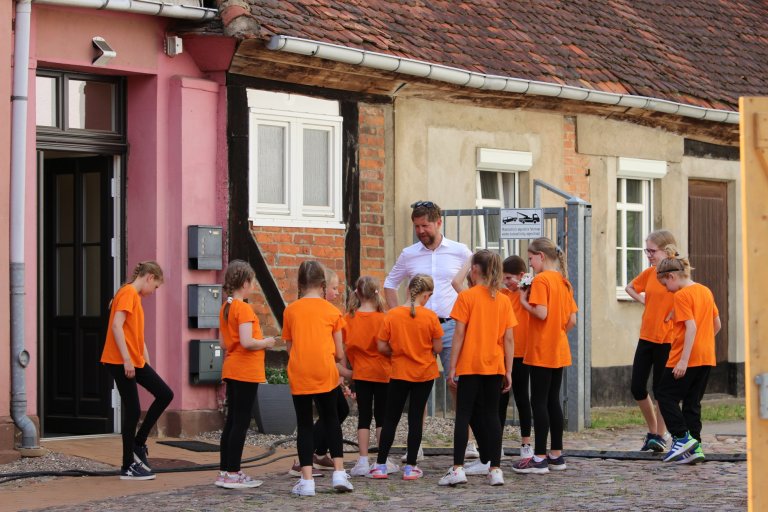 Musikschulgruppe in orangenen T-Shirts beim Lindenfest Ludwigslust, Kinder und Erwachsener in historischer Altstadt.