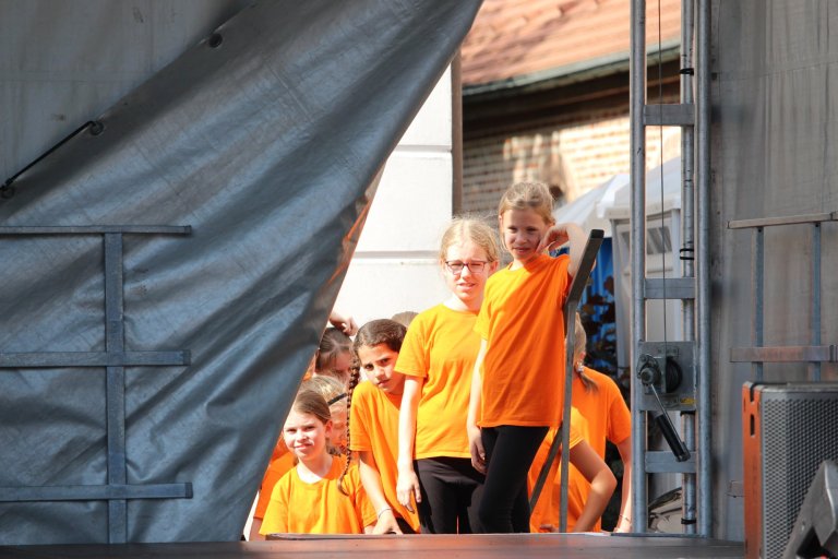 Kinder in orangenen Musicalschul-Shirts auf Bühne beim Lindenfest Ludwigslust, bereit zur Aufführung.