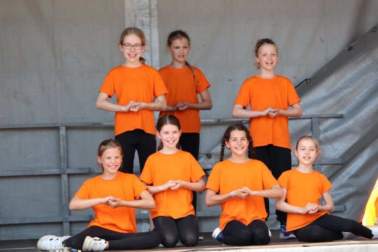 Gruppe von Kindern in orangenen T-Shirts präsentiert Tanzformation beim Lindenfest Ludwigslust der Musicalschule Ahrensburg.