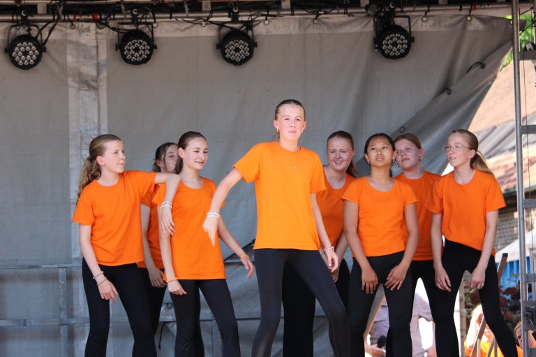 Gruppe junger Performer in orangenen Shirts auf der Bühne beim Lindenfest Ludwigslust der Musicalschule Ahrensburg.